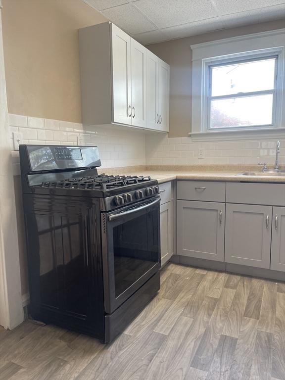 466-470 Cambridge St, Fall River, MA 02721 - kitchen featuring black range with gas cooktop, light wood-style floors, light countertops, backsplash, and a drop ceiling