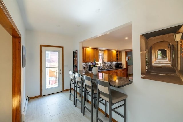 4 Fall St, Malden, MA 02148 - kitchen featuring brown cabinets, dark countertops, backsplash, a sink, and a kitchen breakfast bar
