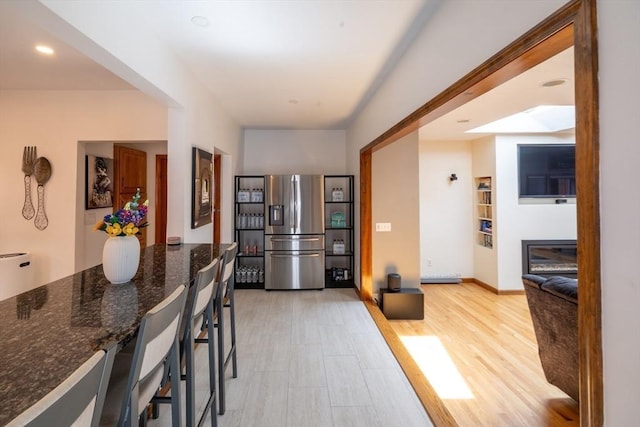4 Fall St, Malden, MA 02148 - kitchen with stainless steel fridge with ice dispenser, dark stone countertops, a kitchen bar, light wood finished floors, and baseboards