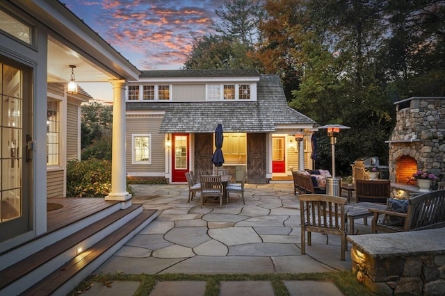 patio terrace at dusk featuring an outdoor stone fireplace