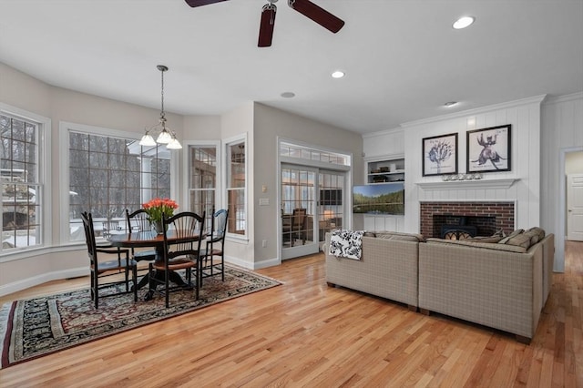 living room with ceiling fan with notable chandelier, a fireplace, built in features, and light hardwood / wood-style floors