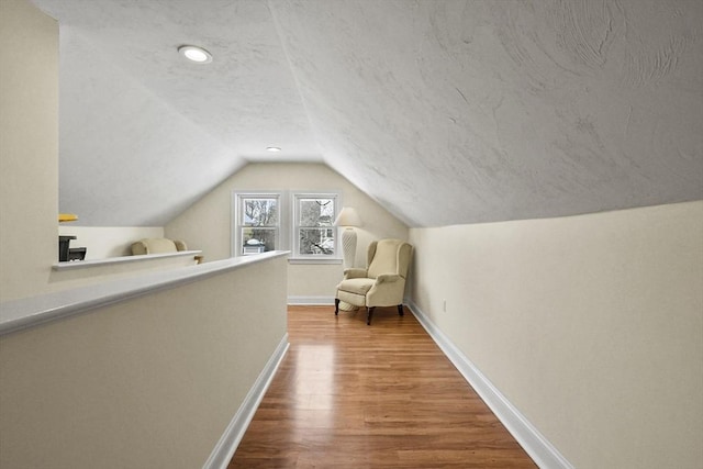 additional living space featuring lofted ceiling, a textured ceiling, wood finished floors, and baseboards