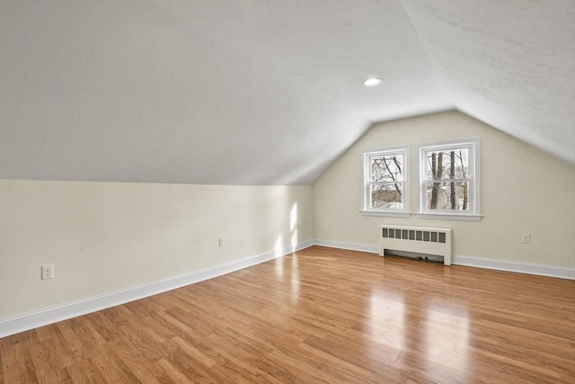 additional living space with radiator heating unit, light wood-type flooring, and baseboards