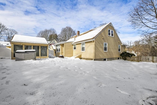 snow covered rear of property featuring a hot tub, a chimney, and fence