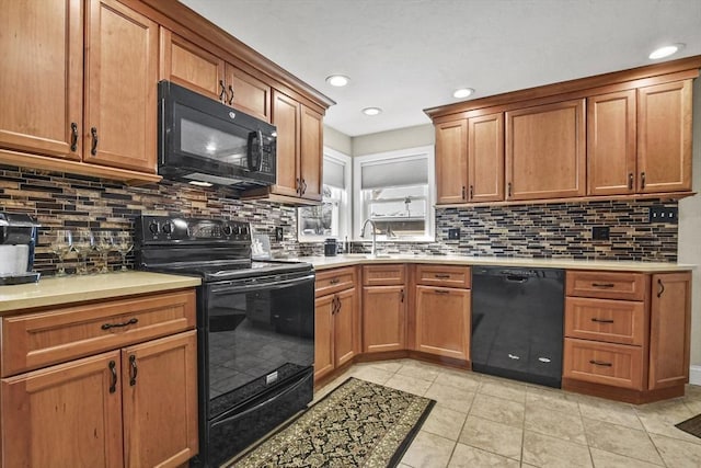 kitchen with light tile patterned floors, light countertops, brown cabinetry, a sink, and black appliances