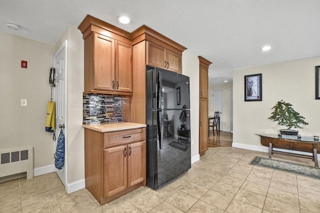 kitchen featuring brown cabinets, radiator, light countertops, decorative backsplash, and freestanding refrigerator