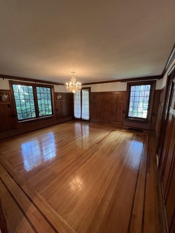 spare room featuring an inviting chandelier, ornamental molding, and light wood-type flooring