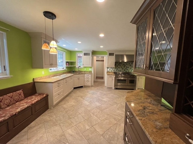 kitchen featuring pendant lighting, white cabinetry, extractor fan, decorative backsplash, and range with two ovens