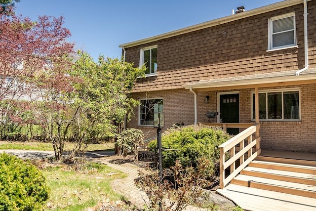 view of front of property with brick siding, a shingled roof, mansard roof, and a porch