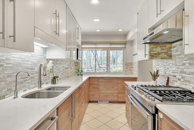 kitchen featuring a sink, gas stove, light countertops, tasteful backsplash, and under cabinet range hood