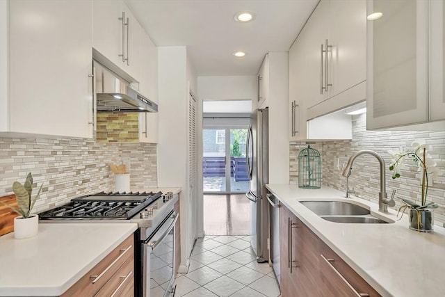 kitchen with light tile patterned floors, under cabinet range hood, a sink, appliances with stainless steel finishes, and backsplash
