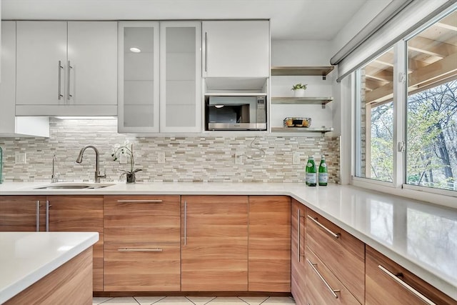 kitchen with light countertops, stainless steel microwave, decorative backsplash, and a sink