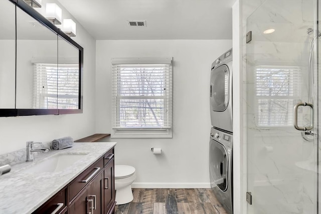 bathroom featuring stacked washing maching and dryer, a marble finish shower, vanity, and visible vents