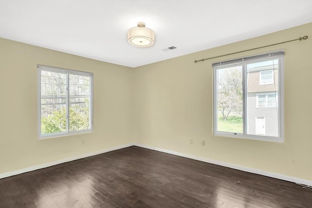 spare room featuring plenty of natural light, dark wood-style flooring, baseboards, and visible vents