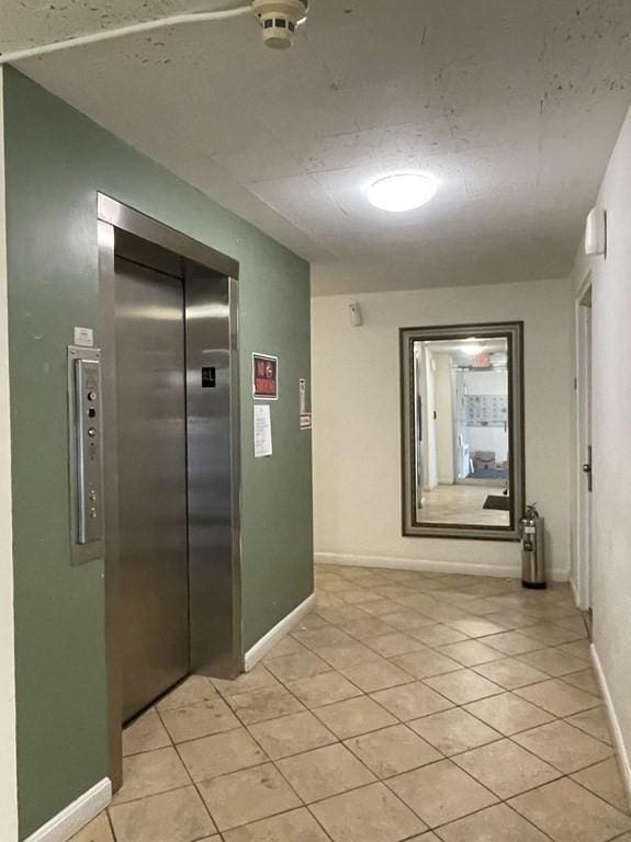 hall with elevator, baseboards, and light tile patterned flooring