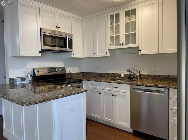 kitchen featuring glass insert cabinets, a peninsula, white cabinets, stainless steel appliances, and a sink