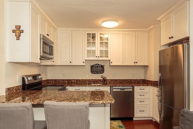 kitchen featuring dark stone countertops, appliances with stainless steel finishes, a peninsula, white cabinets, and a sink