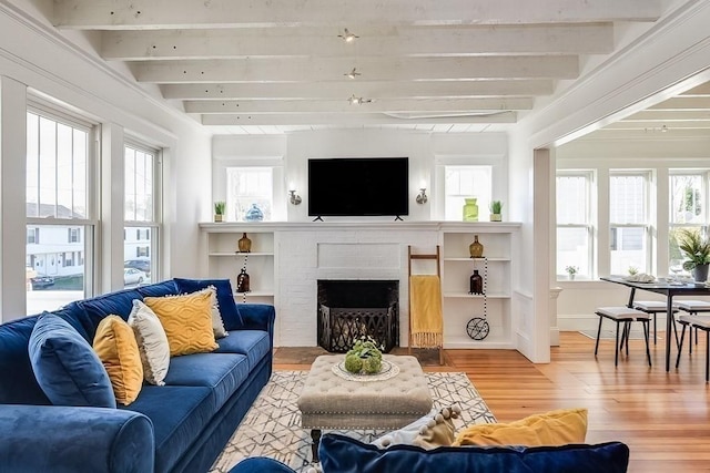 living room with light wood-type flooring, beamed ceiling, plenty of natural light, and a brick fireplace