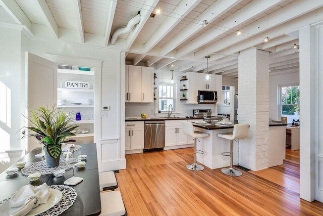 kitchen featuring beam ceiling, light wood-style flooring, dark countertops, white cabinetry, and stainless steel appliances