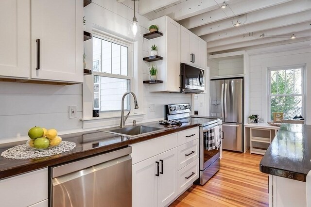 kitchen with a sink, stainless steel appliances, open shelves, and dark countertops