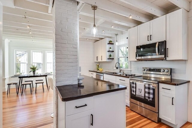 kitchen with light wood finished floors, open shelves, a sink, stainless steel appliances, and beamed ceiling