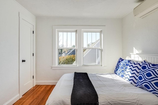 bedroom with a wall mounted air conditioner, baseboards, and wood finished floors