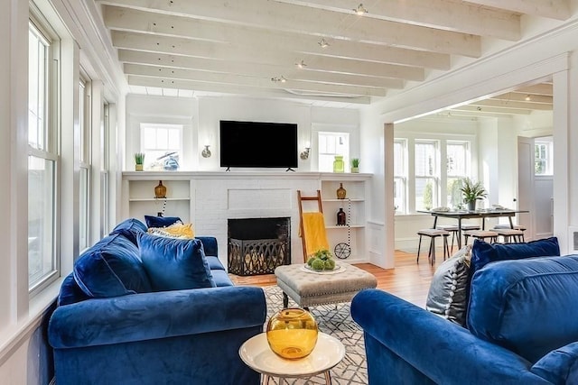 living area with beamed ceiling, a fireplace, baseboards, and wood finished floors