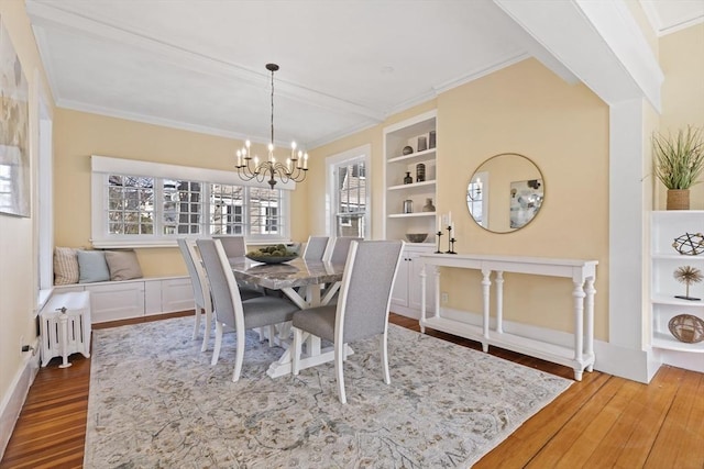 dining space featuring built in features, wood finished floors, baseboards, an inviting chandelier, and crown molding