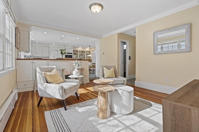 living area featuring wood finished floors, baseboards, recessed lighting, crown molding, and baseboard heating