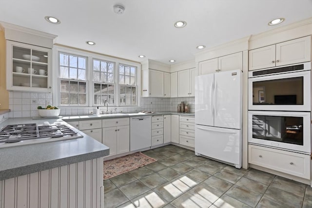 kitchen featuring tasteful backsplash, light countertops, white appliances, white cabinetry, and a sink