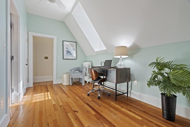 office area with baseboards, lofted ceiling with skylight, a ceiling fan, and light wood finished floors