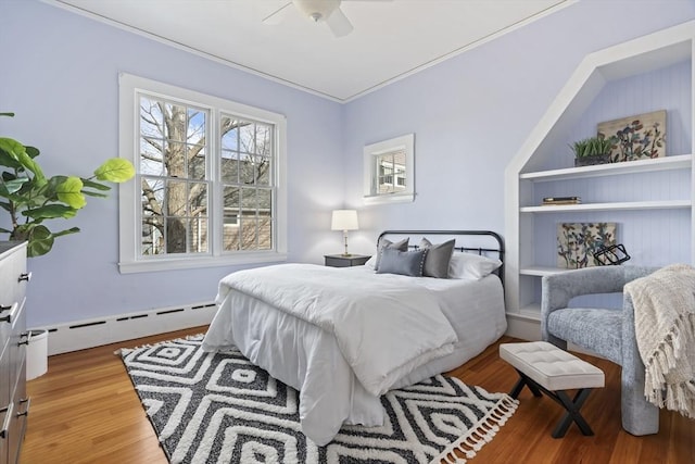 bedroom featuring a baseboard radiator, wood finished floors, a ceiling fan, and crown molding