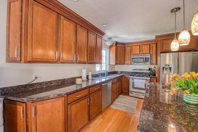 kitchen with appliances with stainless steel finishes, brown cabinets, light wood-style floors, and a sink