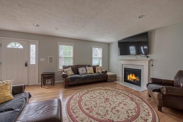 living room with light wood-type flooring, a fireplace, recessed lighting, a textured ceiling, and baseboards