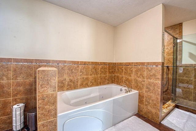 full bathroom with tile walls, a tub with jets, a shower stall, and a wainscoted wall