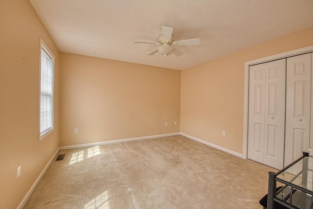 unfurnished bedroom featuring light carpet, baseboards, a closet, and a ceiling fan