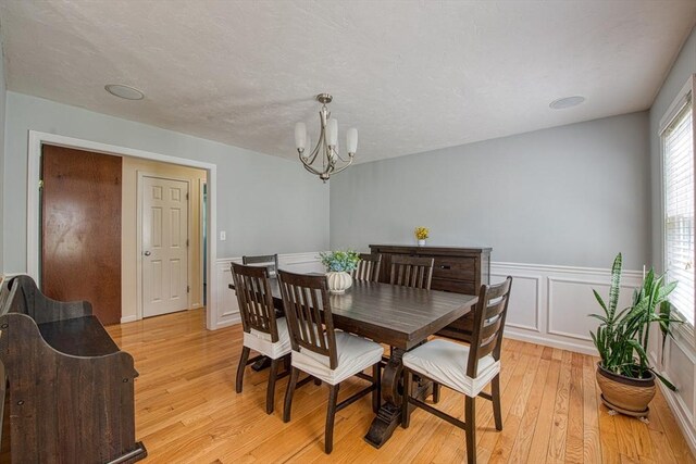 dining space featuring light wood-type flooring, a chandelier, wainscoting, and a decorative wall