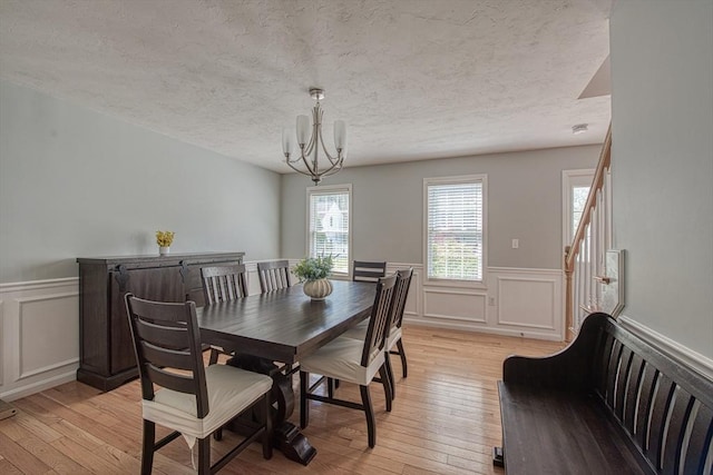 dining room with a chandelier, wainscoting, light wood-type flooring, a textured ceiling, and a decorative wall