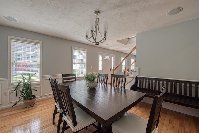 dining room with a chandelier, wainscoting, stairway, light wood-style flooring, and a textured ceiling