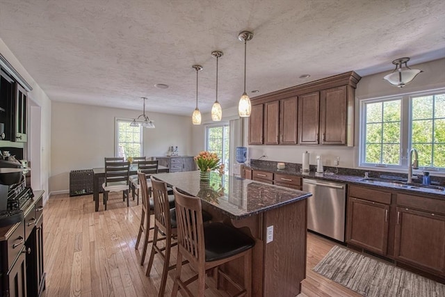 kitchen with stainless steel dishwasher, a sink, plenty of natural light, light wood-style floors, and a textured ceiling