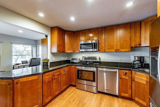 24 Shore Rd, Southwick, MA 01077 - kitchen featuring appliances with stainless steel finishes, brown cabinets, light wood finished floors, a peninsula, and a textured ceiling