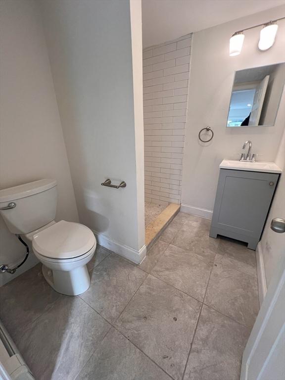 bathroom with tile patterned flooring, vanity, toilet, and a tile shower