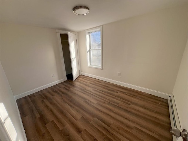 unfurnished room featuring baseboard heating and dark hardwood / wood-style flooring