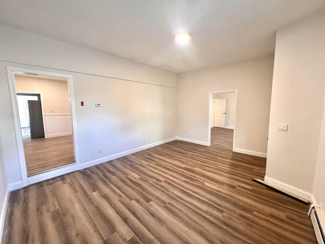 empty room with dark hardwood / wood-style floors and a baseboard heating unit