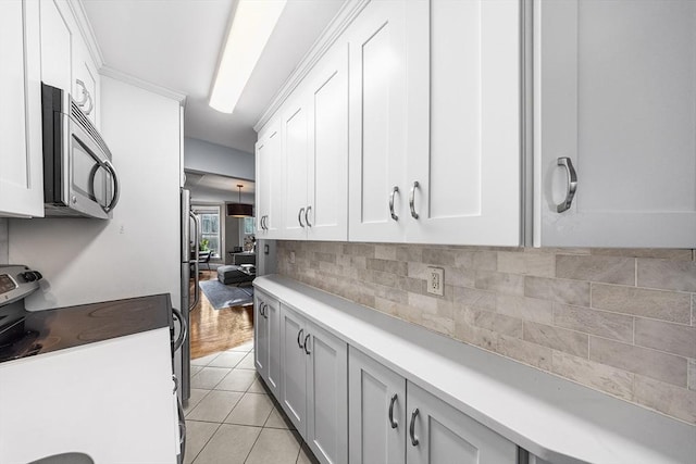 kitchen featuring electric stove, light tile patterned flooring, light countertops, white cabinets, and backsplash