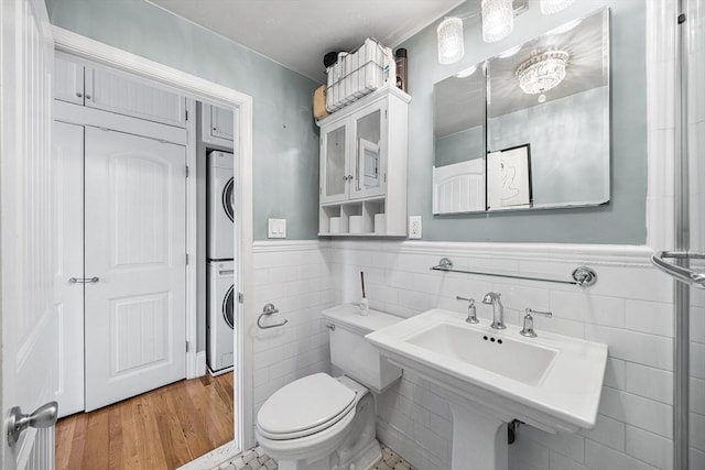 bathroom featuring a wainscoted wall, toilet, tile walls, wood finished floors, and stacked washer / drying machine