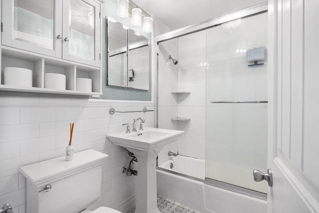 bathroom featuring tile walls, enclosed tub / shower combo, and toilet