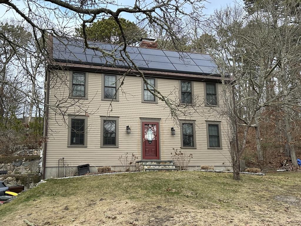 colonial-style house featuring a front yard and solar panels