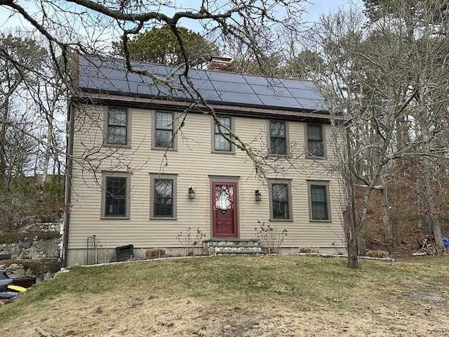 colonial house featuring a front lawn and solar panels