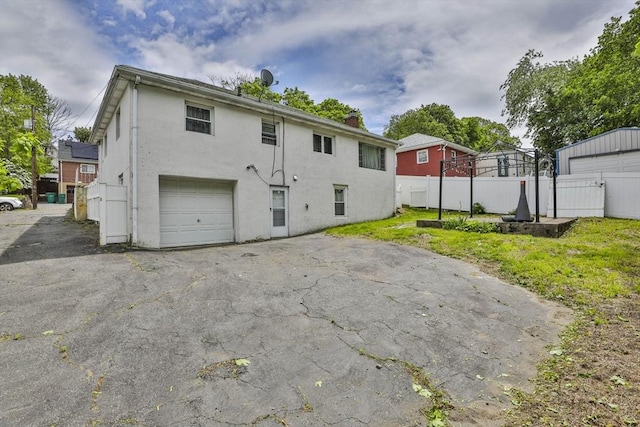 35 Linden Ter, Lynn, MA 01902 - back of property featuring a garage, fence, stucco siding, asphalt driveway, and a chimney